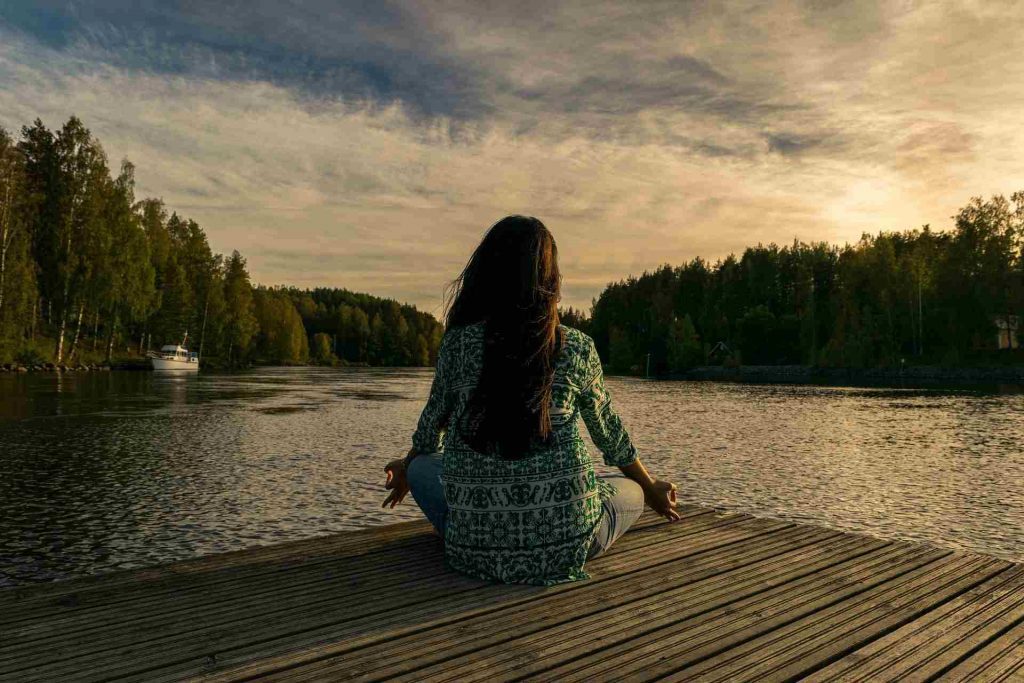 Mujer meditando para reducir la ansiedad frente a un lago 