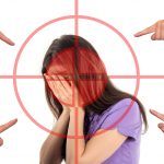 Mujer que siente ansiedad se tapa la cara al ser señalada con la manos por varias personas.