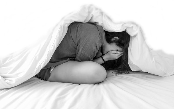 Mujer con trastorno de estrés postraumático (tipo de trastorno de ansiedad) se esconde debajo de las sábanas.